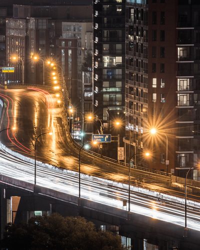 Glowing light streaks from a wet Gardiner Expressway as traffic never stops. Hot & rainy, muggy summer night in Lakeside Toronto Ontario, Canada.